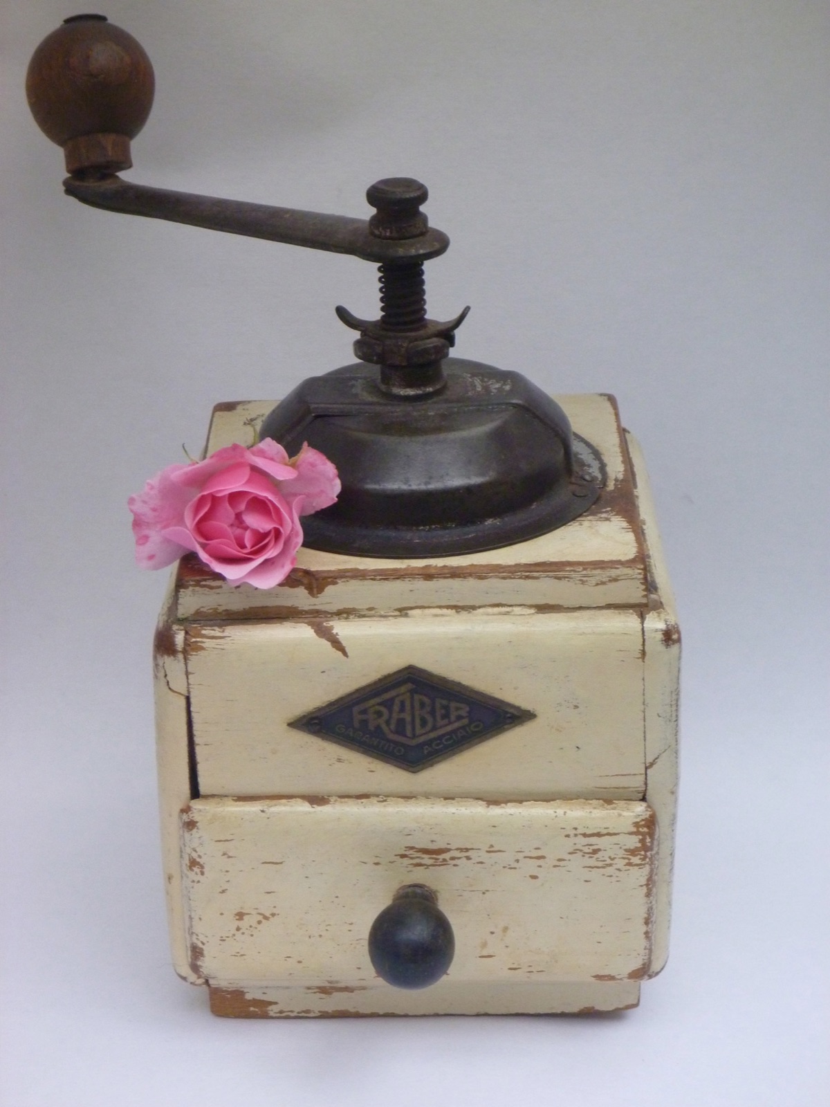 An antique wooden coffee grinder with a pink rose resting on top